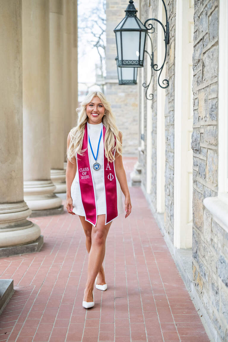 Grad photo of PSU student in white dress with red store and medal at Old Main 